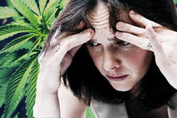 woman holding head looking anxious on cannabis leaf background